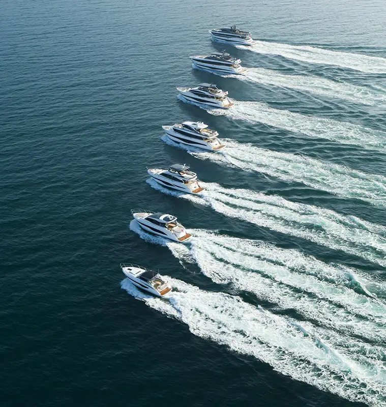 Luftaufnahme einer Formation von Luxusyachten in Österreich, die mit hoher Geschwindigkeit über das klare blaue Meer fahren und weiße Wellen hinter sich lassen. Die perfekt ausgerichteten Yachten erzeugen ein beeindruckendes Bild von Präzision und Geschwindigkeit auf dem offenen Wasser.