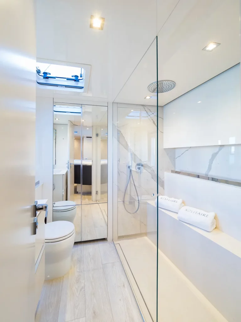 A bright, luxurious bathroom on the Sunreef 50 yacht, with a glass-enclosed shower, modern fixtures, and light-colored finishes, including a skylight.