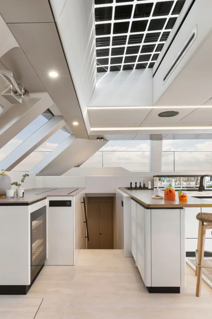 ine moderne Küche an Bord der Sunreef Power 60P Eco Yacht, ausgestattet mit einer zentralen Insel, modernen Geräten und einer stilvollen Bar mit Sitzgelegenheiten. Das Design verbindet Luxus mit Nachhaltigkeit.