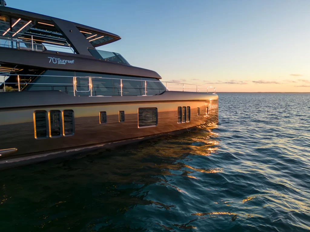Seitlicher Blick auf die 70 Sunreef Power bei Sonnenuntergang, mit ihrem glänzenden, reflektierenden Rumpf, der das goldene Licht einfängt.