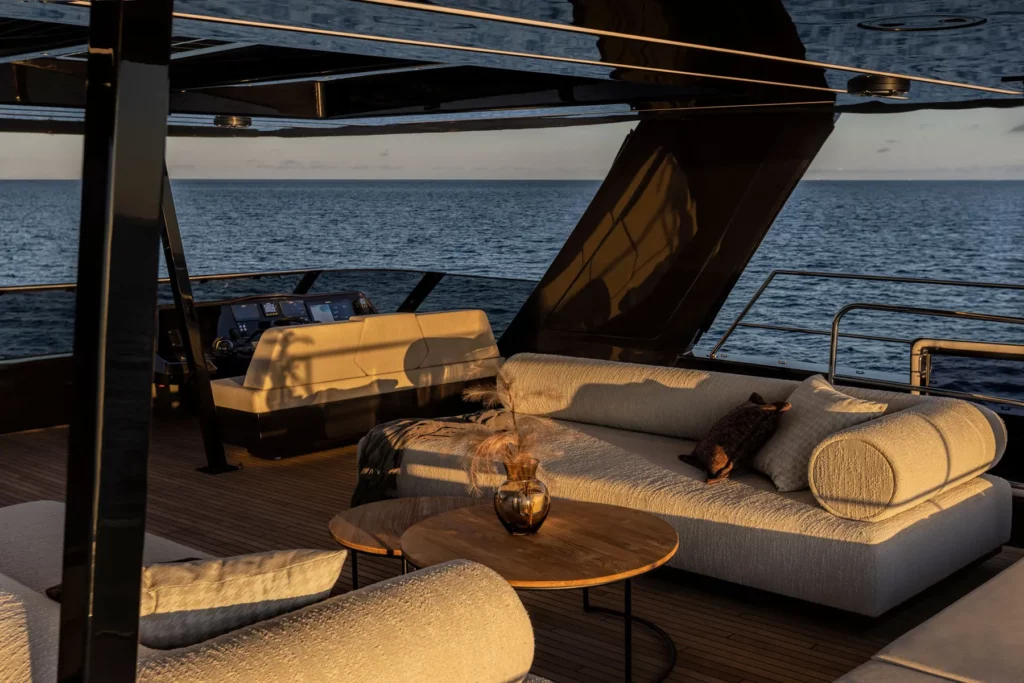 Die Flybridge des 70 Sunreef Power Katamarans bei Sonnenuntergang, ausgestattet mit eleganten Sofas und einem Steuerstand, der einen weiten Blick auf das Meer bietet.