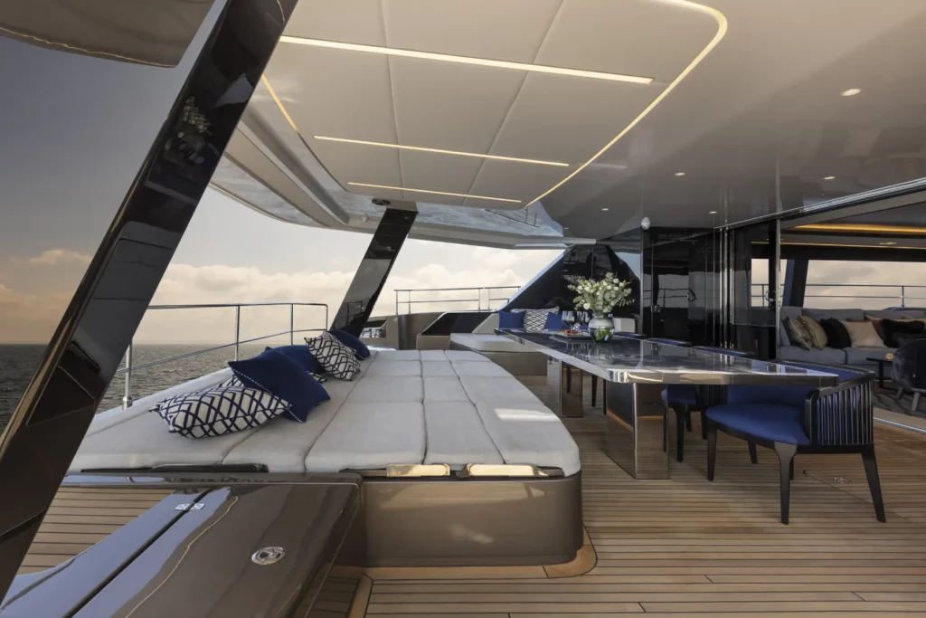 Das geräumige Außendeck der 80 Sunreef Power Yacht, mit gepolsterten Sonnenliegen mit dunkelblauen Kissen, einem eleganten Esstisch für Mahlzeiten im Freien und einem modernen Design mit klaren Linien und Blick auf den Ozean.