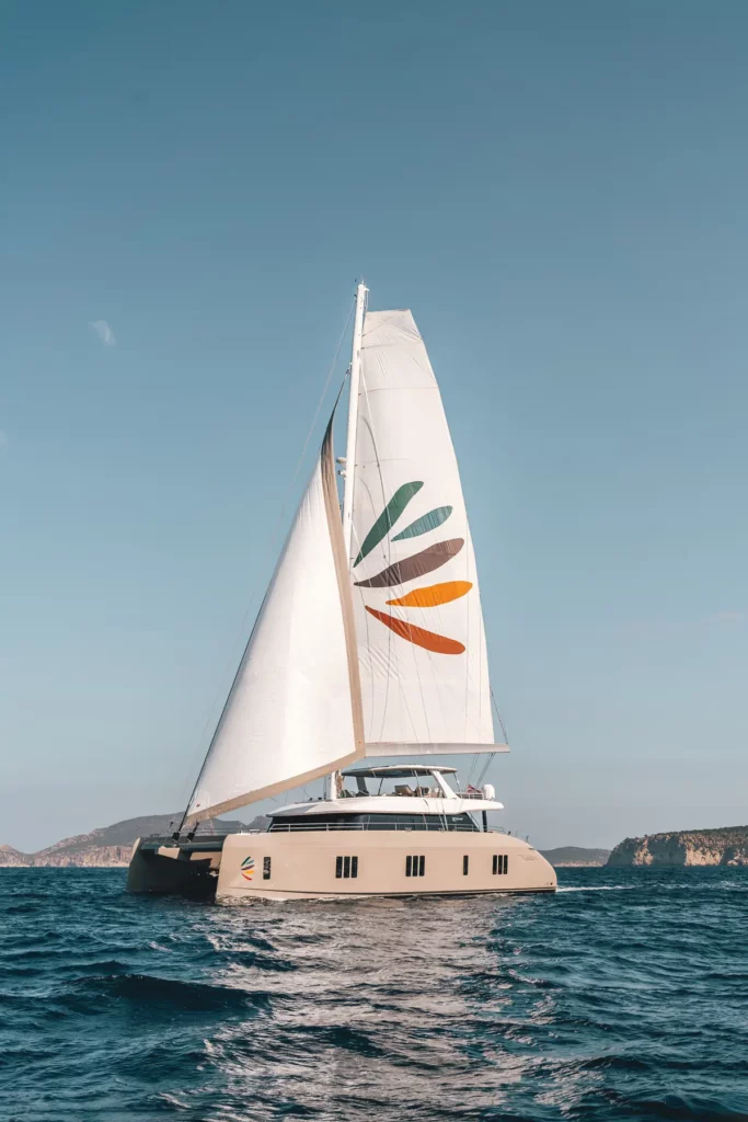 Seitenansicht eines Sunreef 80 Katamarans unter Segeln, das Design der Yacht ist modern und elegant, mit Bergen im Hintergrund.