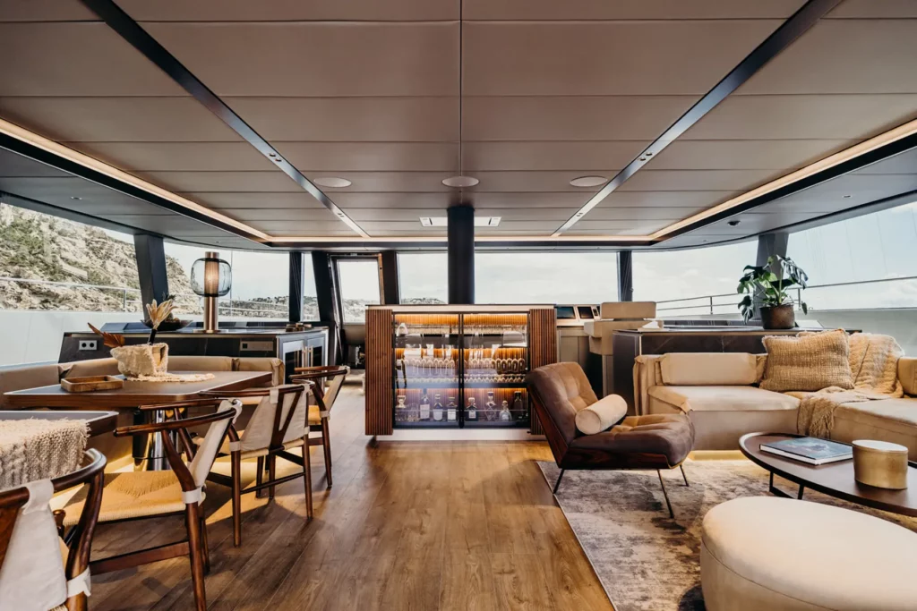 Luxuriöser Salon auf dem Sunreef 80 Katamaran mit modernem Design, Holzboden und gemütlichen Sitzbereichen, sowie einer eleganten Bar mit beleuchtetem Flaschenschrank.