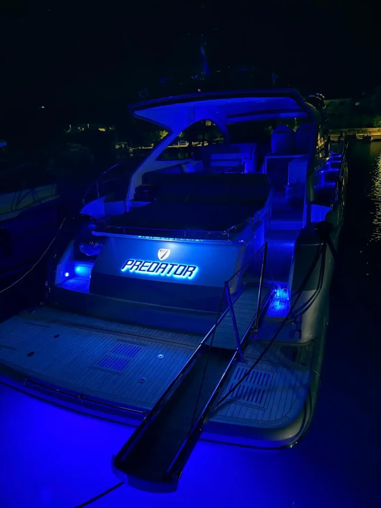 Nächtliche Heckansicht der Fairline Targa 48 Open mit atmosphärischer blauer Beleuchtung und beleuchtetem Bootsnamen „Predator“.