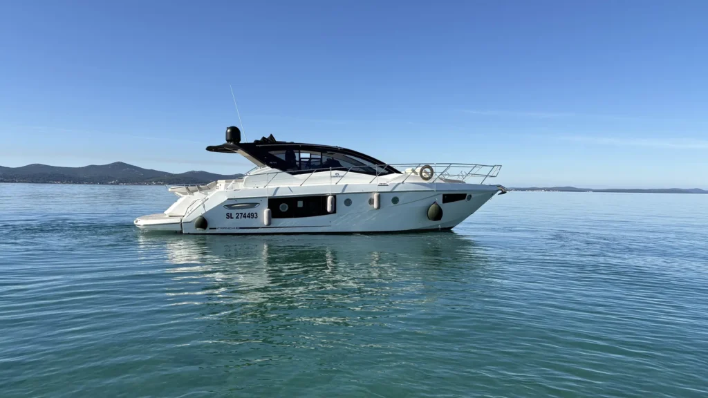 Cranchi M44 Motoryacht in Seitenansicht auf ruhigem Meer vor einer Inselkulisse unter blauem Himmel.