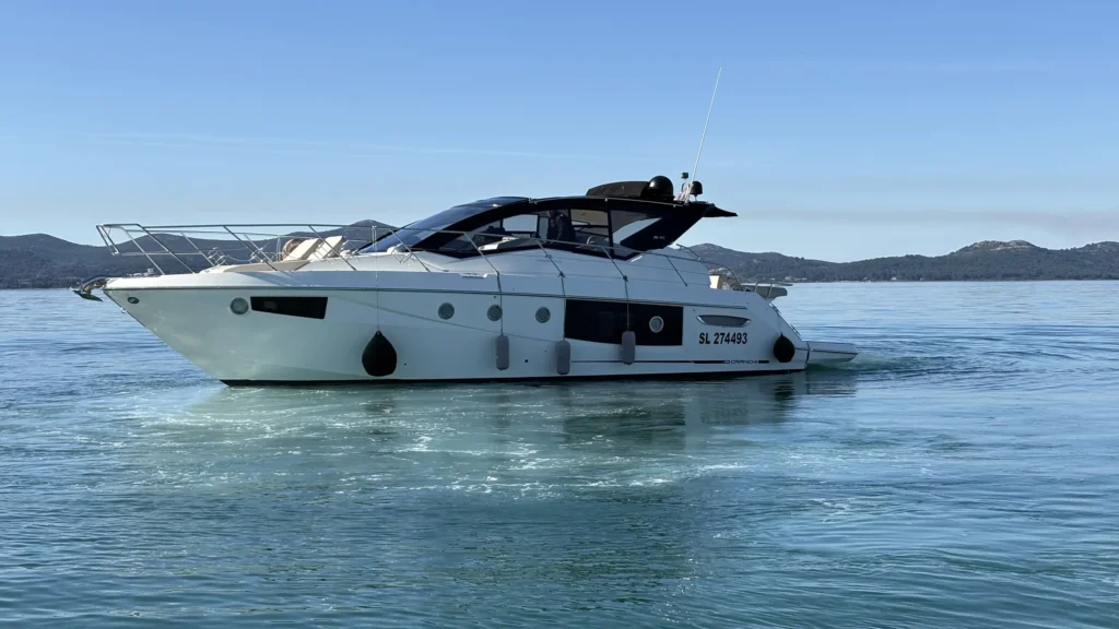 Cranchi M44 in Seitenansicht auf glattem Wasser, mit sanften Hügeln und Küstenlinie im Hintergrund.