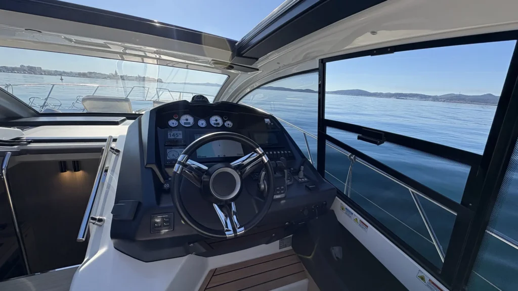 Cockpit der Cranchi M44 mit Fahrerplatz und Sitzbank, seitlich große Fenster mit Meerblick.