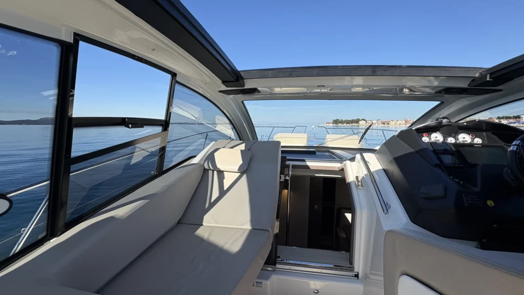 Cockpit-Innenansicht der Cranchi M44 nach vorn mit Sitzbank, Abgang nach unten und Küstenblick durch die Frontscheibe.