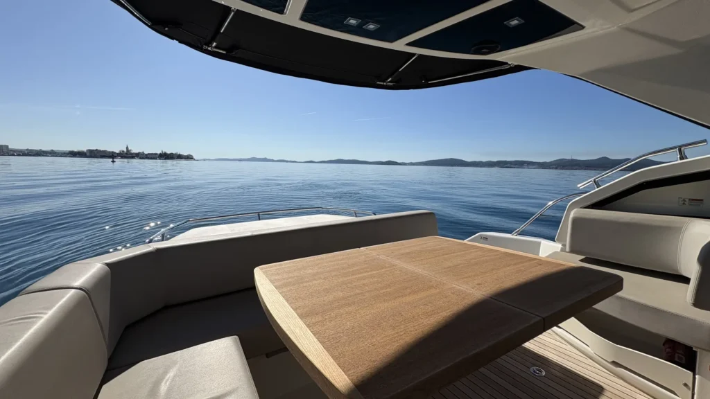 Hecklounge der Cranchi M44 mit Holztisch und U-Sitzbank, dahinter glitzerndes Meer und Inseln.