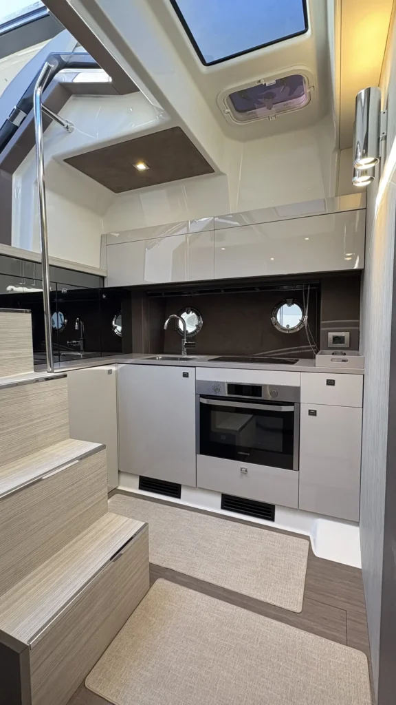 Pantry der Cranchi M44 mit Treppe, Spüle, Kochfeld und Backofen, beleuchtet durch Deckenfenster.