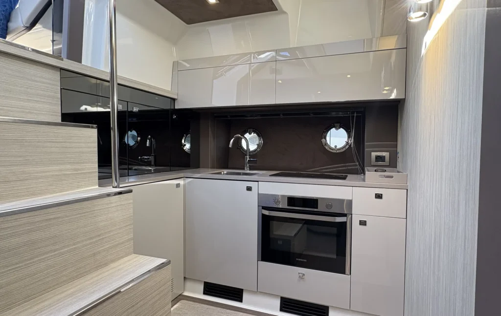 Detail der Pantry in der Cranchi M44 mit Spüle, Induktionskochfeld und Bullaugen über der Arbeitsfläche.