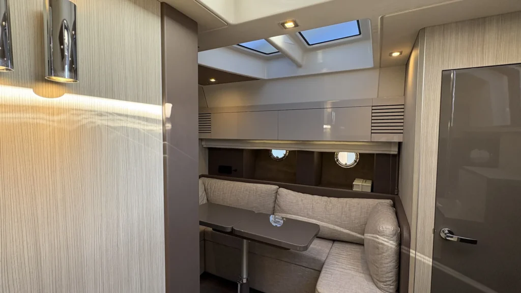 Salon der Cranchi M44 mit L-Sitzbank, Tisch, Oberlicht und zwei Bullaugen, Blick aus dem Kabinengang.