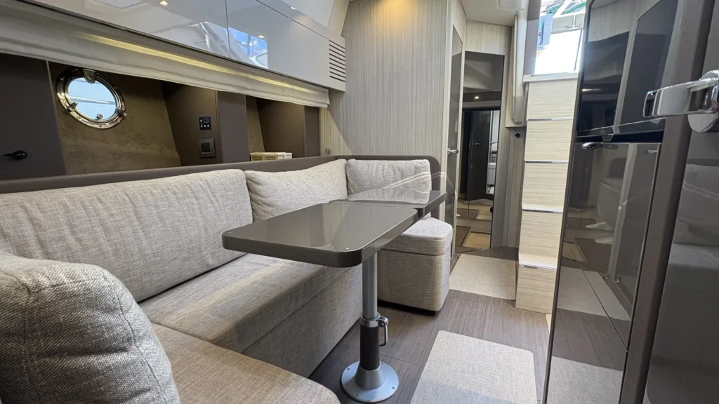 Salon der Cranchi M44 mit langer Sitzbank und Tisch, rechts Hochglanz-Schrankfront, Blick Richtung Kabinenbereich.